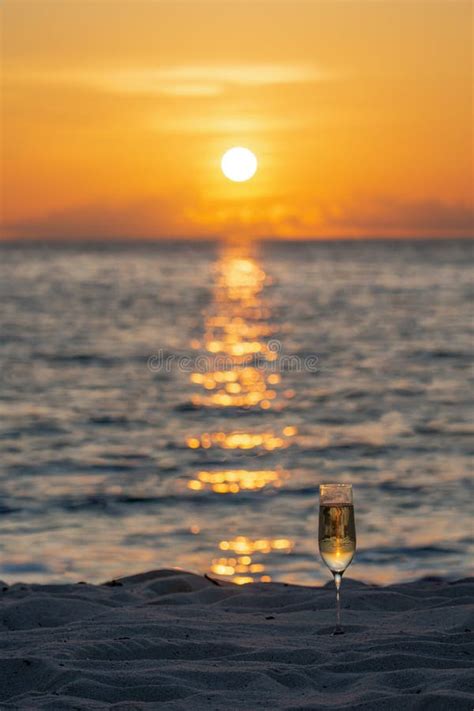 A Wine Glass With Liquid Is In The Sand On The Beach Stock Photo