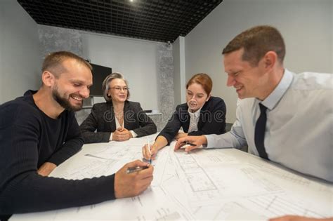 Four Business People Sitting Around A Table Discussing Blueprints