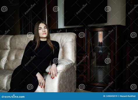 Young Pretty Cute Brunette Sitting On A White Sofa In The Living Room