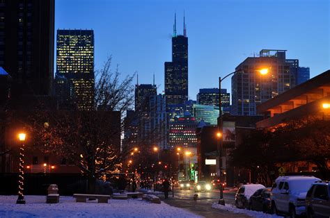 A City Street At Night With Snow On The Ground And Buildings Lit Up In