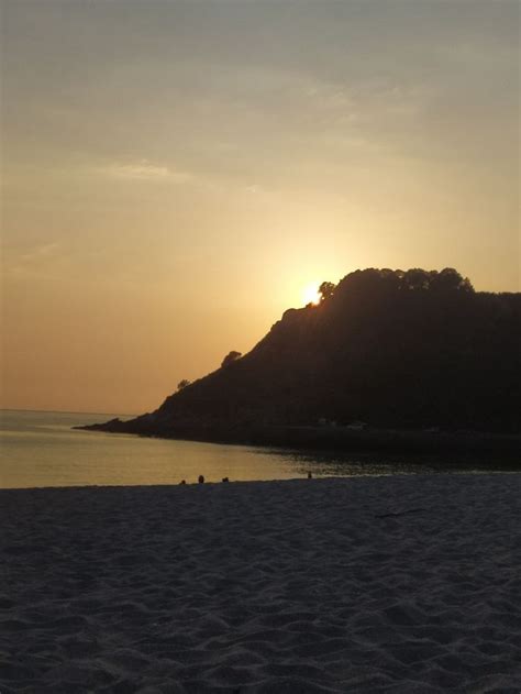 The Sun Is Setting Over An Island In The Ocean With People Sitting On