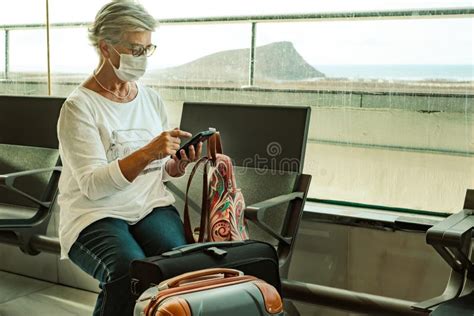 Senior Female Traveler Sitting In Airport With Luggages Using Mobile