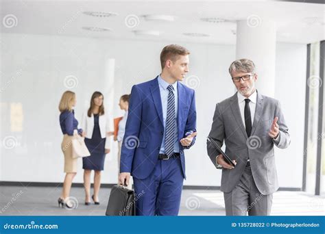 Businessmen Discussing While Walking Against Colleagues At Office Stock