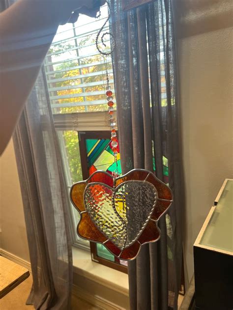 A Stained Glass Heart Hanging From The Side Of A Window In Front Of A