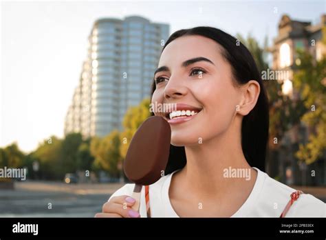 Beautiful Young Woman Eating Ice Cream Glazed In Chocolate On City