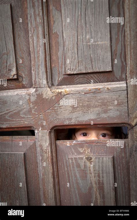 A Toddler Looks Through A Small Crack In An Old Wooden Door Revealing