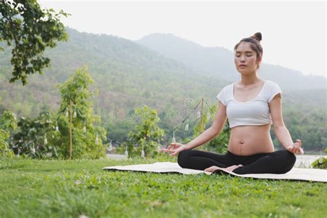 Asian Pregnant Woman Practicing Yoga While Sitting In Lotus Position On