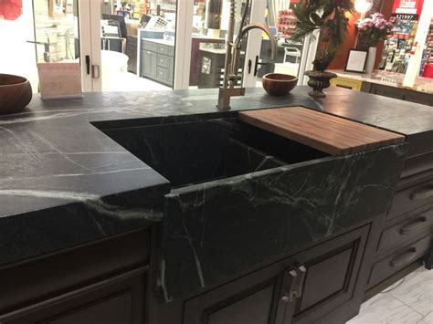 A Kitchen Sink With Black Marble Countertops And Wooden Cabinets In