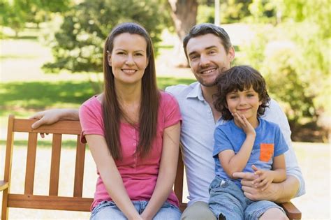 Sonriente Pareja Con Hijo Sentado En El Banco Del Parque Foto Premium