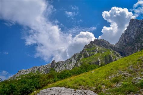 some rocks and grass on the side of a mountain with clouds in the sky above