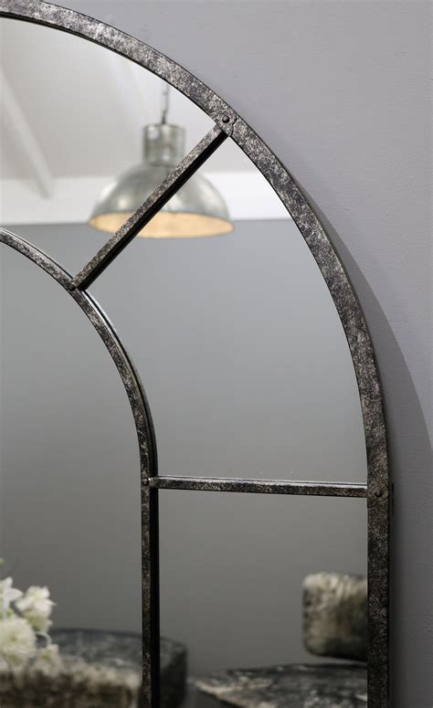 An Arched Mirror Hanging On The Wall Next To A Table With Flowers In