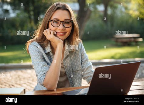 Smiling Brunette Woman In Eyeglasses Sitting By The Table In Park With