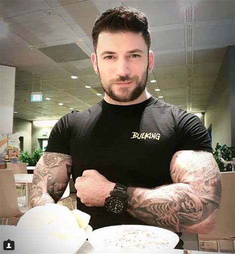 A Man With Tattooed Arms Standing In Front Of A Plate Of Food And