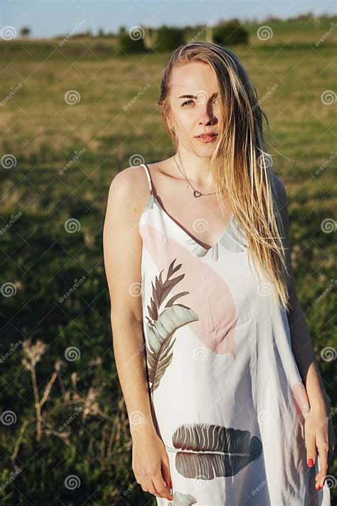 Blonde Woman Walking Through A Green Field At Sunset Stock Photo