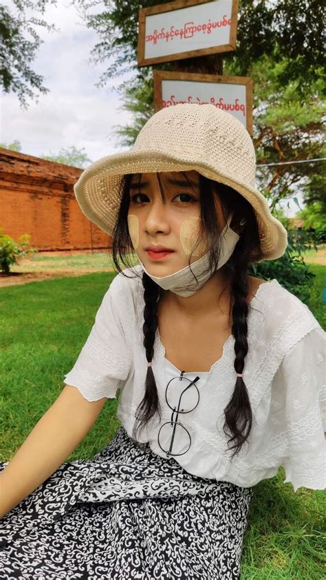 A Woman Sitting In The Grass With A Hat On Her Head And A Sign Behind Her