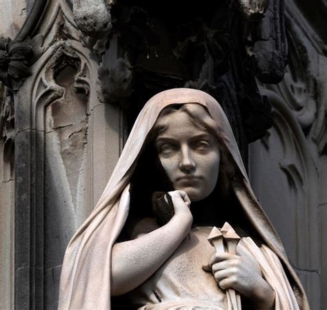 Una estatua de una mujer con una cruz en la cabeza está de pie frente a