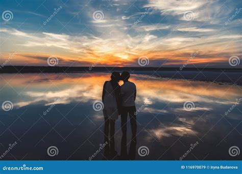 Portrait Silhouette Of Happy Couple Watching The Colourful Bright Sunset Standing In Large Lake