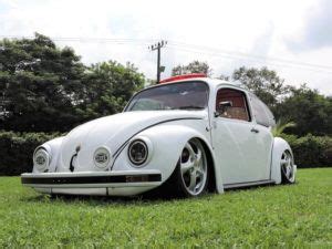 A White Vw Bug Parked On Top Of A Lush Green Field