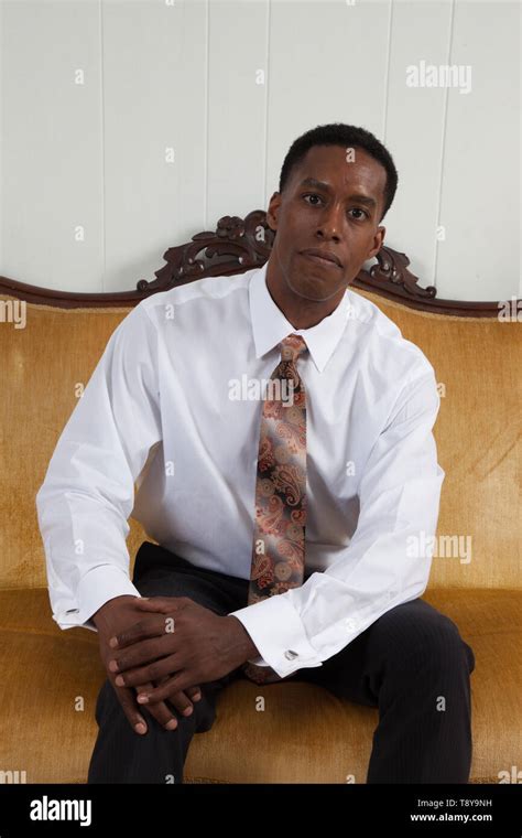 Handsome Black Man In A White Shirt And Tie Sitting On A Gold Couch