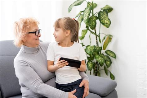 Abuela feliz y nieta usando el teléfono juntas sentadas en un cómodo