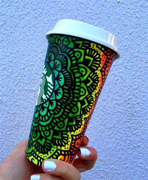 A Hand Holding A Starbucks Cup With An Intricate Design On The Lid And