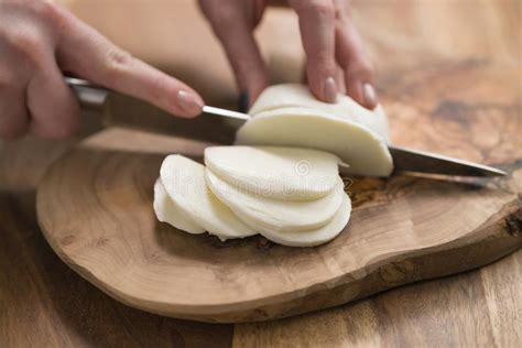 Female Teen Hand Slicing Mozzarella Cheese With Knife On Wooden Board