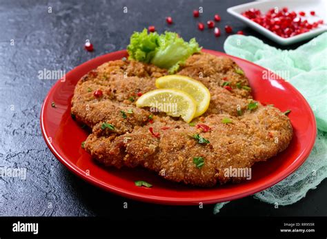 Gran schnitzel vienés en una placa roja con limón sobre un fondo negro