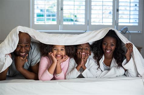 Familia Feliz Que Miente Debajo De Una Manta En Cama Foto De Archivo