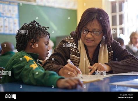 A Female Teacher Shows A Young African Girl How To Write In A Classroom