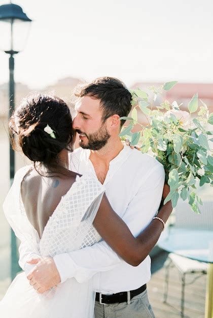 Premium Photo Groom Hugs Bride With A Bouquet Of Flowers On The Roof