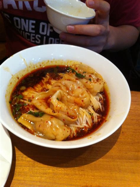 A White Bowl Filled With Noodles And Sauce Sitting On Top Of A Wooden