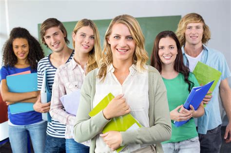 College Boy Holding Books With Blurred Students In Park Stock Photo