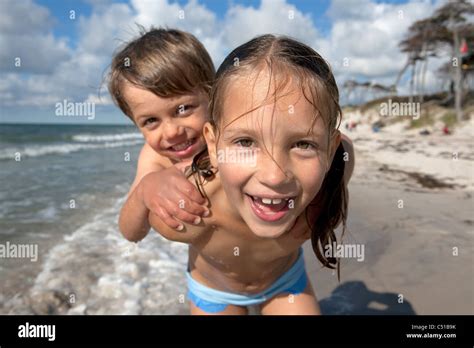 portrait of young girl giving piggyback ride to little brother on the beach Stock Photo - Alamy