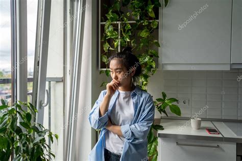 Chica asiática milenaria pensativa mirando por la ventana pensando en