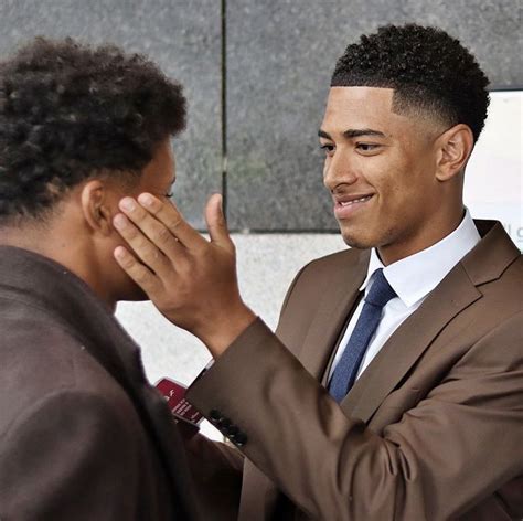 Two Men Standing Next To Each Other And One Is Touching His Face With