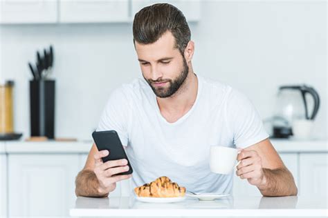 아침 식사 하는 동안 스마트폰 사용 하 여 잘생긴 수염된 젊은이 가정 생활에 대한 스톡 사진 및 기타 이미지 가정 생활