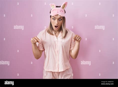 Blonde Caucasian Woman Wearing Sleep Mask And Pajama Pointing Down With