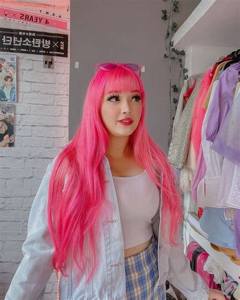 A Woman With Long Pink Hair Standing In Front Of A Rack Of Clothes And Looking At The Camera