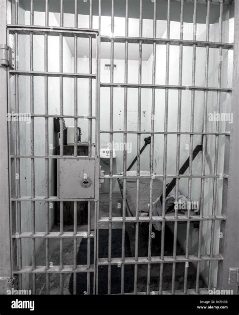 Old jail cell view through the steel bars showing bed and sink Stock Photo - Alamy