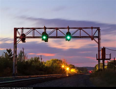 Two Green Traffic Lights Are Hanging Over The Train Tracks At Dusk