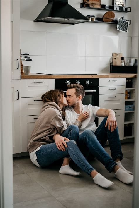 A Man And Woman Sitting On The Floor In Front Of An Oven Kissing Each Other