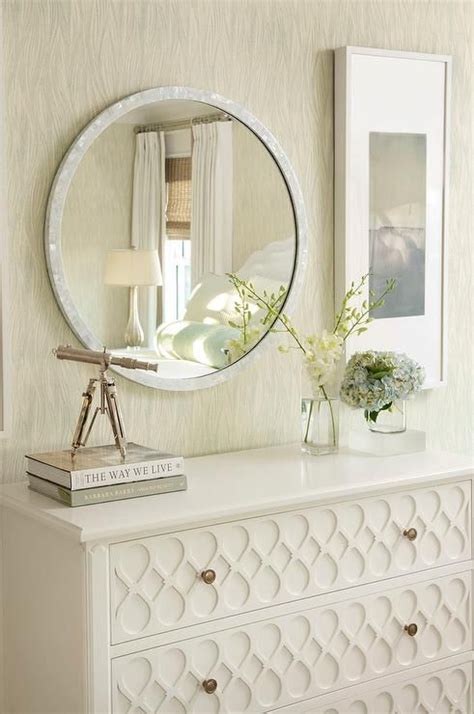 Round White Capiz Mirror Above A White Dresser With Ornate Overlay Trim