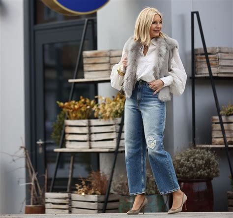 A Woman Is Standing On The Sidewalk Wearing Jeans And A Fur Vest With