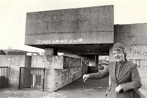 A Woman Standing In Front Of A Concrete Building With Graffiti On Its