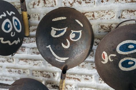 Old Frying Pans With Painted Faces Hang On A Brick Wall Stock Photo