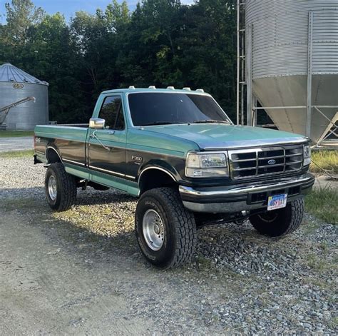 A Green Pick Up Truck Parked In Front Of A Silo