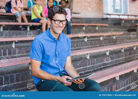 Portrait Of Teacher Sitting On Bench And Using Digital Tablet Stock