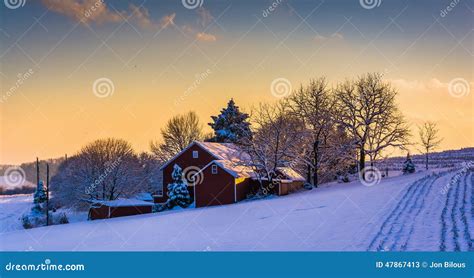 Winter View Of A Barn On A Snow Covered Farm Field At Sunset In Stock