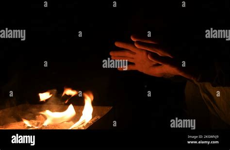 Close Up In Complete Darkness A Man Warms His Hands On An Open Fire