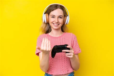 Jeune fille anglaise blonde jouant avec un contrôleur de jeu vidéo isolé sur fond jaune invitant